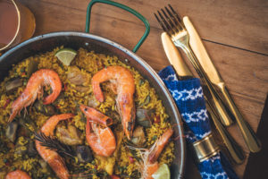 Paellapfanne mit Meeresfrüchten und goldenem Besteck und blauer Batikserviette für entspannte Geburtstagsfeier